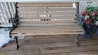Full view of the garden bench showing the metal decorative sides and wooden slats for seating and backrest. The bench is placed on a wooden deck surface.