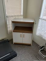 Front view of white and wood cart with shelf and two doors below, showing condition and design.