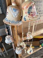 Four terra cotta wind chimes hanging, showing various painted faces, sun designs, and geometric patterns in earthy painted colors