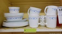 Shelf display of Corningware Blue Cornflower pattern plates, bowls, and mugs.