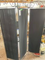 Straight-on view of three-panel folding room divider showing black cloth panels with metal frames and decorative scrollwork at the top.