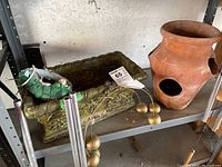 Photo of garden accessories on metal shelf including terra cotta pot, green ceramic planter, and wind chimes