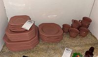 Stack of brown square dinner plates, salad plates, and bowls in the corner with price tags on top of plates