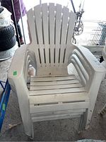 Four white resin Muskoka chairs stacked and standing next to each other, showing wear marks, scuffs, and dirt.