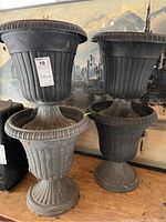 Four black plastic pedestal planters stacked in pairs, showing size and general condition with some dirt visible inside.