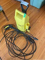 Yellow Marcher power washer unit with long black hose and spray gun coiled on a wood floor.