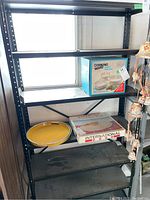 Full view of black metal shelving unit showing several shelves with some kitchenware items which are excluded from sale.