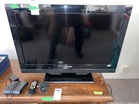 Front view of Sony Bravia 32in TV on wooden stand with power cord, remote, and another cord beside it.