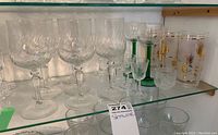 Various clear and etched wine, liqueur, and sherry glasses with decorative drinking glasses on glass shelf