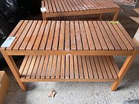 Front view of wooden slatted side table with lower shelf on concrete floor.