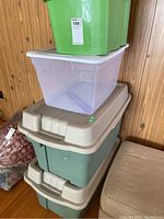 Stacked view of four plastic storage totes. From top to bottom: green, white translucent, and two beige totes, all with lids. Shows size differences, colors, and general condition.