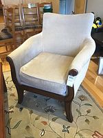 Front left angle view of beige upholstered armchair with dark wood frame