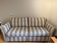 Front view of the couch showing the full length, seat and back cushions, and armrests with geometric square patterned upholstery in neutral tones.