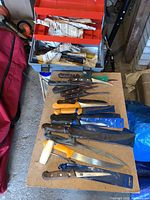 Image showing an open tackle box with knives wrapped in paper inside and various butcher knives laid out on a board.
