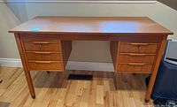 Full view of teak desk with two banks of three drawers and tapered legs