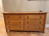Front view of a wooden dresser showing six drawers with wooden knobs.