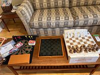 Overview of multiple games including onyx chess set, glass chess board, magnetic dart board with darts, and card sets (Uno and Rummy-O) placed on table in front of couch.