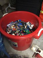 Wide view of large red tub filled with assorted LEGO bricks and minifigure parts inside plastic bags