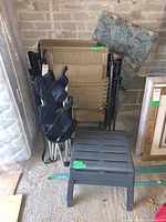 Two beige mesh plastic seating patio loungers with metal frames, navy blue foldable lawn chair, black plastic foot rests, and floral garden chair cushion in storage setting.