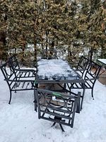Full view of black metal framed patio table with glass top and six matching chairs outdoors in snow