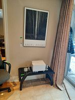 Framed Ansel Adams print hanging on the wall beside a window and a black wood bench below it holding miscellaneous items (not included).