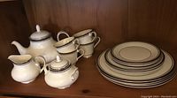 Overall view of the Royal Doulton Sara Bande tea set with plates, cups, teapot, sugar bowl and creamer arranged on wooden shelf.