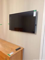 Samsung flat screen TV mounted on wall with remote control placed on wooden cabinet.