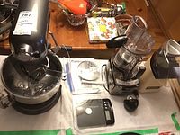 All four appliances on table: stand mixer with bowl and whisk, digital scale, Cuisinart attachments, and popcorn maker