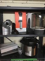 Wide shelving view showing Instant Pot on bottom shelf, Anova Precision Cooker in box, Yonanas attachments, and Sunbeam humidifier on top shelf.