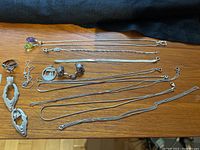 Photo showing an assortment of sterling silver jewelry laid on a wooden surface including necklaces, earrings shaped like birds, a ring, a frog-shaped ring, and the Toronto cityscape pendant.