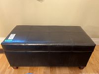 Front view of the black faux leather storage bench with cushioned lid and visible stitching.