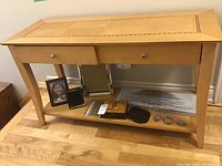Front view of light wood hall table with inlay tabletop, showing two drawers and lower shelf with various items (not included) placed on it.