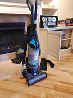 Full view of the upright vacuum cleaner standing on wooden floor near fireplace.