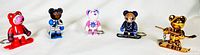 Five bear figurines on a white cloth background, all in standing pose with skis or hockey sticks, viewed from the front.