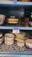 Shelf with large popcorn bowl marked 'Love that Popcorn' on left, CorningWare dishes in middle and right, and various small bowls and plates below