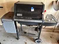 Photo of a black Weber Silver propane grill with side burner and front wheels on a concrete floor.