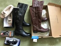 Photo showing two pairs of tall boots: brown leather HH Bass & Co boots with buckle on side, black leather Naturalizer boots with three buckles, plus Nautica moccasin slippers with faux fur lining, sunglasses, and compression socks on carpeted floor.