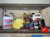 Photo showing gallon containers of Berkebile antifreeze coolant, Zerex antifreeze coolant, Rain-X 2-in-1 cleaner, and various yellow microfiber rags on a metal shelf.