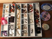 Overhead view of jewelry organizer trays with various necklaces, bracelets, and earrings and small trinket dishes on a wooden table.
