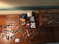 Wide shot of assorted costume jewelry including earrings, pins, bracelets, two wristwatches and storage boxes placed on wooden surface