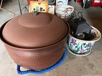 Large hammered metal pot with lid featuring a small bird-shaped handle, sitting on blue braided pad.