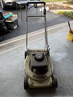 Weathered Cub Cadet push lawnmower with metal handlebars and plastic base visible.