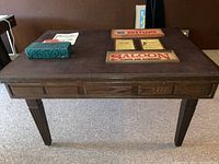 Closed view of the brown table with bar style signs on top and a manual, showing fluted legs and storage drawer at the front