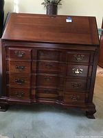Front view of wood secretary desk showing four drawers with brass handles and slant front closed.