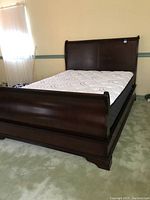 Front view of assembled queen-size dark wood sleigh bed with mattress and box spring