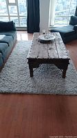 Area rug placed under a rustic wooden coffee table between sofas in a living room with city view windows.