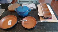 Photo showing blue Denby cast iron pot with lid, two copper frying pans, wooden cutting board and various serving trays.
