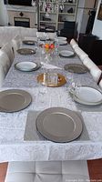 Full dining table set with plates, chargers, glasses, placemats and tablecloth