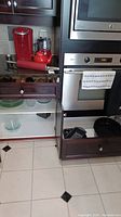 Wide shot showing red Keurig coffee maker, mini food processor, rolling pin on countertop, glass pie plates inside cabinet, stainless steel roasting pan in drawer below microwave oven.