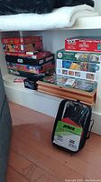 Stacked board games Risk, Star Wars Risk, assorted puzzles in colorful boxes on floor shelf with ping pong kit case nearby